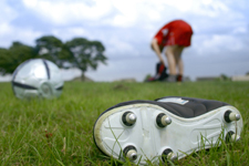 football/rugby boot lying on grass in foreground, with field and player behind